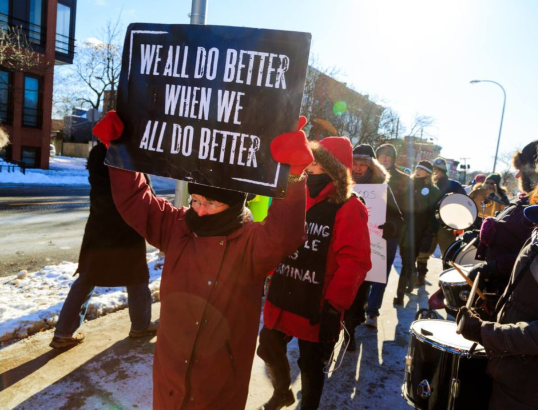 An activist holding a "we all do better when we all do better" sign.
